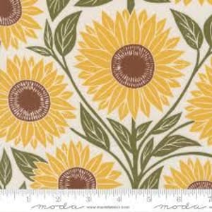 May include: A fabric with a repeating pattern of sunflowers in shades of yellow and brown, set against a cream background. Green leaves and stems intertwine with the flowers. A ruler is at the bottom.