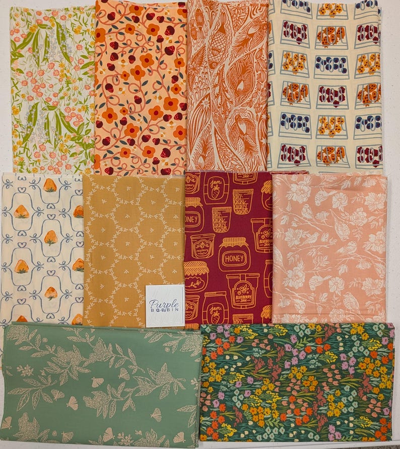 Pu&ograve; includere: Una collezione di campioni di tessuto con vari disegni floreali e a motivi. I colori includono arancione, giallo, verde e rosa. Alcuni tessuti presentano fragole, barattoli di miele e dettagliate illustrazioni botaniche. Il logo "Purple Bobbin" &egrave; visibile.