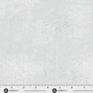 May include: A light gray fabric with a speckled pattern and vertical brushstroke texture. The fabric has a ruler along the bottom edge with the Andover logo and website address.