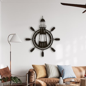 Puede incluir: Una pieza de arte mural de metal marrón oscuro con un faro. El faro está centrado dentro de un diseño de timón. La obra de arte está montada en una pared blanca en un salón.