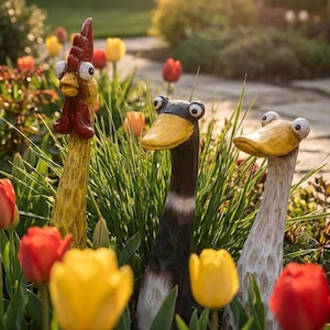 May include: Three garden sculptures shaped like long-necked birds. The left figure is a yellow rooster with a red comb. The middle figure is a black bird with a yellow beak. The right figure is a white bird with a yellow beak. All have large eyes.