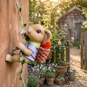 May include: A charming garden ornament depicting a rabbit ascending a rope, with a basket of carrots. The rabbit is dressed in a light blue shirt and green scarf. The statue is set against a brick wall, with a garden scene in the background.