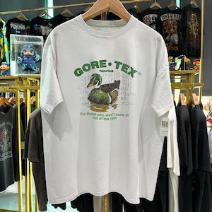 Puede incluir: Camiseta blanca con un gráfico de pato verde y marrón, las palabras "GORE-TEX fabrics" y la frase "For those who won't come in out of the rain". La camiseta es de manga corta.