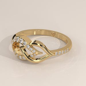 Può includere: Un anello in oro lucido caratterizzato da un intricato design a nodo traforato sulla parte anteriore. La fascia e il motivo centrale a nodo sono impreziositi da piccole pietre rotonde e trasparenti incastonate a pavé. Un piccolo marchio è visibile.