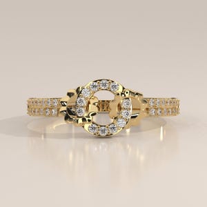 May include: A gold ring featuring a central circular motif adorned with small round white stones. The band is split into two parallel rows, each set with a continuous line of small round white stones that extend around the finger.