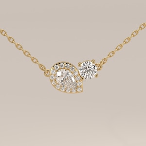 May include: A gold chain necklace featuring a pear-shaped diamond pendant surrounded by a halo of small round diamonds, positioned next to a single round brilliant-cut diamond, all set in a polished yellow gold metal frame and delicate chain.