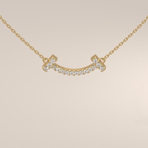 May include: A gold chain necklace featuring a curved, smile-shaped pendant. The pendant is crafted from yellow gold and is set with a row of small, clear, round-cut diamonds that follow the arc of the design, attached to a delicate gold chain.