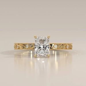 May include: A yellow gold ring featuring a large rectangular radiant-cut center diamond held by four prongs. The band is decorated with an intricate engraved leaf pattern and small round accent diamonds set at intervals along the shank.