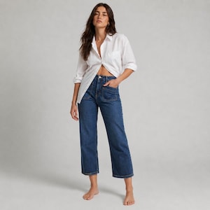 May include: A crisp white long-sleeved button-down shirt with a classic collar and front placket, paired with dark blue denim jeans featuring a high-waisted fit, straight-leg cut, and prominent patch pockets on the front hips.