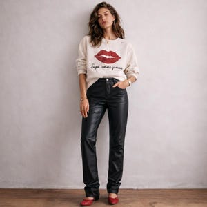 May include: A woman wearing a cream-colored sweatshirt with a large red sequined lips design and the text "Sapé comme jamais". She is also wearing black leather pants and red flats.