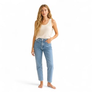 May include: A woman wearing a cream-colored ribbed tank top and light blue denim jeans. The jeans have a high waist and a straight leg. The model is standing in front of a white background.