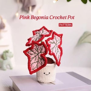 May include: A crocheted pink begonia plant in a white pot. The leaves have red edges and pink and green details. The pot has a smiling face. The text "Pink Begonia Crochet Pot" and "PATTERN" are visible.