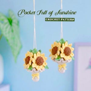 Puede incluir: Dos ramos de girasoles de ganchillo colgantes con centros marrones, pétalos amarillos y hojas verdes. Cada ramo está envuelto en tela gris claro con un pequeño lazo amarillo. El texto dice Pocket Full of Sunshine CROCHET PATTERN.
