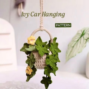 May include: Crocheted hanging car decor featuring a small beige pot filled with green ivy and yellow flowers. The pot hangs from a beige rope. The text "Ivy Car Hanging" is visible above the pot, and the word "PATTERN" is in a green box.