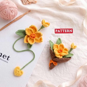 Puede incluir: Dos diseños de flores de narciso de ganchillo hechos a mano. Las flores son amarillas con centros naranjas y hojas verdes. Una flor está unida a un tallo verde con un extremo en forma de corazón amarillo. La palabra "PATTERN" está en un rectángulo rojo.