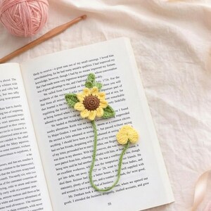 Puede incluir: Marcap&aacute;ginas de girasol de ganchillo hecho a mano con flor amarilla y hojas verdes, sobre un libro abierto. Un accesorio encantador para los amantes de la lectura, que a&ntilde;ade un toque artesanal a la lectura.