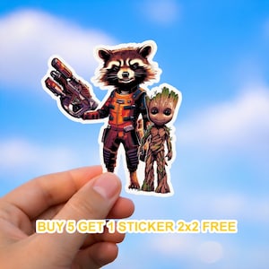 May include: A sticker featuring Rocket Raccoon holding a weapon and Groot. Rocket is in a red and orange outfit. Groot is a brown tree-like character. The sticker is held against a blue sky background. Text at the bottom reads "BUY 5 GET 1 STICKER 2x2 FREE".