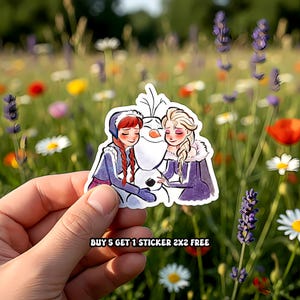 May include: A sticker featuring Anna, Elsa, and Olaf from the movie Frozen. Anna and Elsa are embracing Olaf, the snowman. The sticker has a white border and the text "BUY 5 GET 1 STICKER 2X2 FREE".