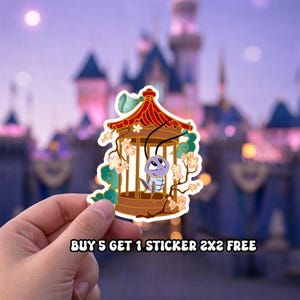 May include: A sticker featuring a cartoon cricket inside a decorative cage with a red and gold roof, adorned with flowers and green accents. The sticker has the text "BUY 5 GET 1 STICKER 2X2 FREE" at the bottom. The background is a blurred image of a castle.
