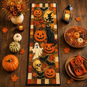 May include: A rectangular quilted table runner featuring a Halloween theme with appliqued pumpkins, a black cat, a ghost, a skull, bats, and a witch silhouette against a background of autumn leaves, bordered by a patchwork of orange and brown squares.