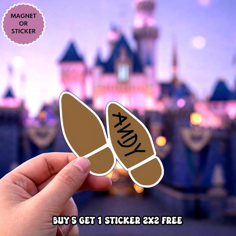 May include: Two brown boot-shaped stickers or magnets with a white border. One boot is plain brown, and the other features the name ANDY written in black capital letters. The items are held against a blurred background of a castle at twilight.