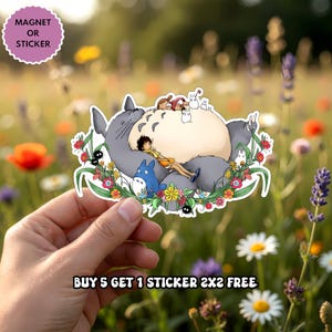 Puede incluir: Una pegatina o im&aacute;n troquelado que muestra un Totoro grande de color gris con vientre crema, un Totoro azul m&aacute;s peque&ntilde;o y una figura humana descansando encima, rodeados de flores coloridas y duendes del polvo, con el texto MAGNET OR STICKER.