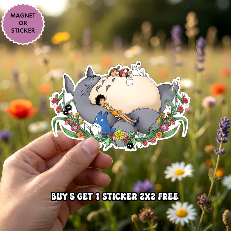 Puede incluir: Una pegatina o im&aacute;n troquelado que muestra un Totoro grande de color gris con vientre crema, un Totoro azul m&aacute;s peque&ntilde;o y una figura humana descansando encima, rodeados de flores coloridas y duendes del polvo, con el texto MAGNET OR STICKER.