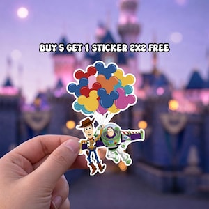 Op de afbeelding: Een sticker met Woody en Buzz Lightyear uit Toy Story, met een cluster van Mickey Mouse-vormige ballonnen. De sticker heeft de tekst "BUY 5 GET 1 STICKER 2X2 FREE" bovenaan. De achtergrond is wazig.
