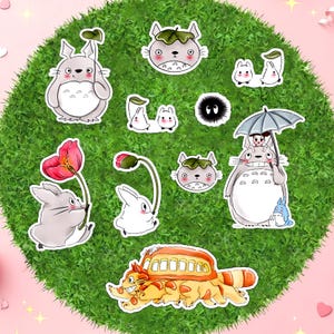 May include: A collection of vinyl stickers featuring various animated characters, including a large grey creature holding a leaf, a cat-shaped bus, small white spirits, a black soot sprite, and a grey creature holding a large umbrella with a small figure.