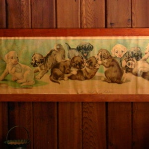 May include: A vintage framed print of a group of playful puppies in various poses. The puppies are brown, black, and white, and they are all looking at the viewer. The print is set against a wood-paneled background.