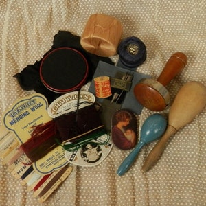Puede incluir: Surtido de suministros de costura y reparación vintage que incluyen carretes de hilo, botones, dedal y un martillo de madera.