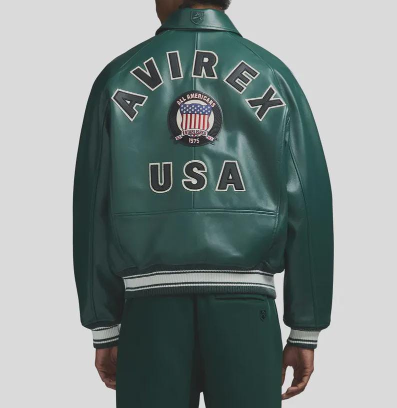 May include: Green leather jacket with white and black striped cuffs and hem. The back of the jacket features the word "AVIREX" in white, arched above a circular patch with the American flag and the words "ALL AMERICANS" and "USA".