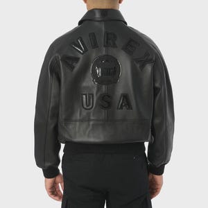 May include: Black leather bomber jacket with the word "AVIREX" arched across the back, above a circular emblem and the word "USA". The jacket has a ribbed hem and cuffs, and a collared neckline.