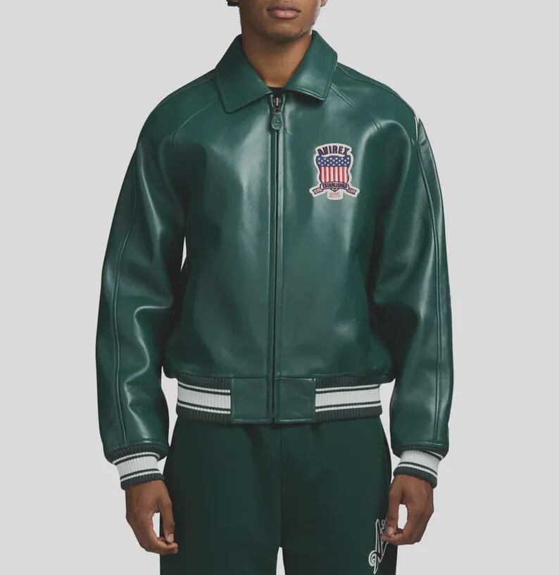 May include: A green leather jacket with a zip-up front, a collar, and a patch on the chest. The jacket has white and gray striped cuffs and a matching hem. The patch features a shield design with the text "AVIREX".