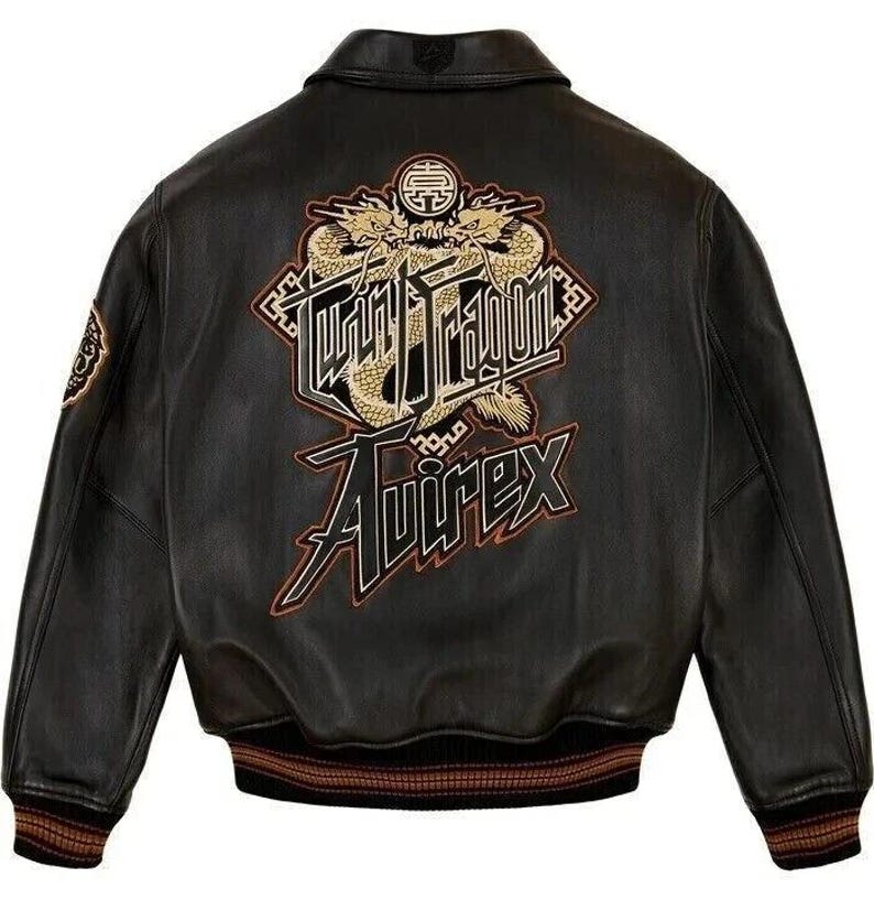 May include: Black leather jacket with a classic collar and a ribbed hem. The back features a gold and black embroidered design with the words "Twin Dragon" and "Avirex". The jacket has a patch on the left sleeve.