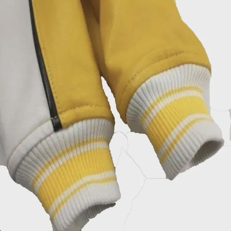 May include: A jacket featuring yellow and white panels separated by a thin black vertical stripe. The sleeves end in ribbed cuffs that are white with two horizontal yellow stripes, providing a distinct contrast to the main body of the garment.