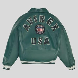 May include: A green leather jacket with the word "AVIREX" arched across the back in white lettering. Below the lettering is a patch with the words "ALL AMERICANS ESTABLISHED 1975" and the USA flag. The word "USA" is below the patch.