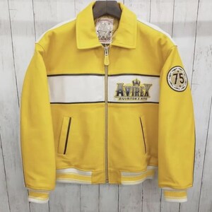 May include: A bright yellow jacket with a white horizontal chest stripe, a full-length front zipper, and ribbed cuffs and hem. The chest features the embroidered text AVIREX AVIATOR'S KING with a crown icon, and a circular patch with the number 75.