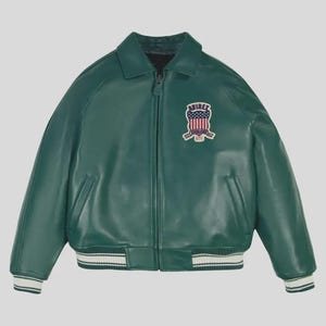 May include: A green leather jacket with a zip-up front, collar, and a patch on the upper left chest. The patch features a shield design with red, white, and blue elements. The jacket has white and black striped cuffs and hem.
