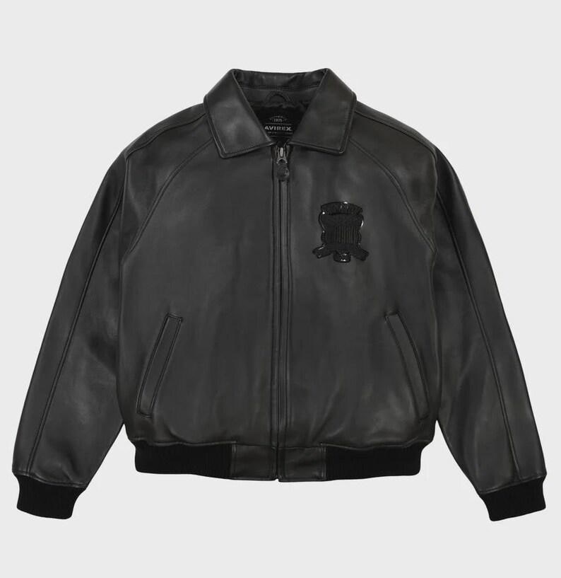 May include: Black leather jacket with a zip-up front, collar, and a black emblem on the chest. The jacket has two front pockets and black ribbed cuffs and hem. The brand name "AVIREX" is visible on the collar.