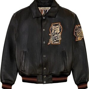 May include: Black leather jacket with a button-up front, featuring a collar and ribbed cuffs. The jacket has embroidered patches with text and a logo, and a brown and gold striped hem. The jacket has two front pockets.
