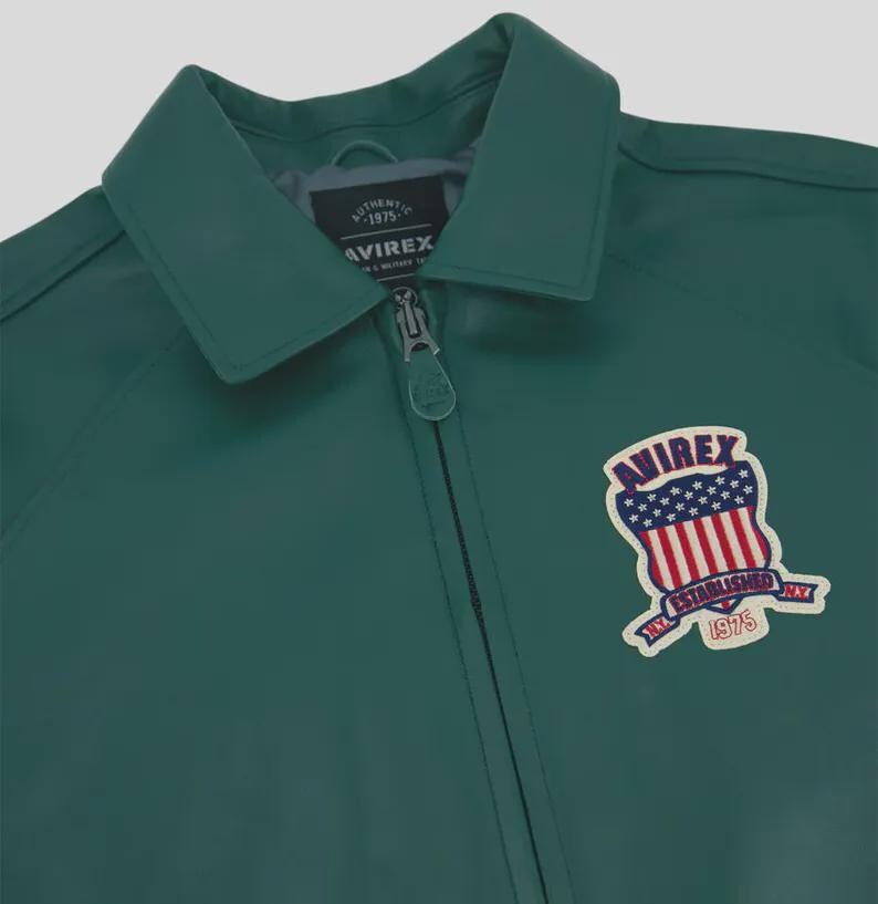 May include: A teal green jacket with a collared neckline and a zipper closure. The jacket features a patch on the front with the text "AVIREX" and an emblem of the American flag. The jacket is a classic style.