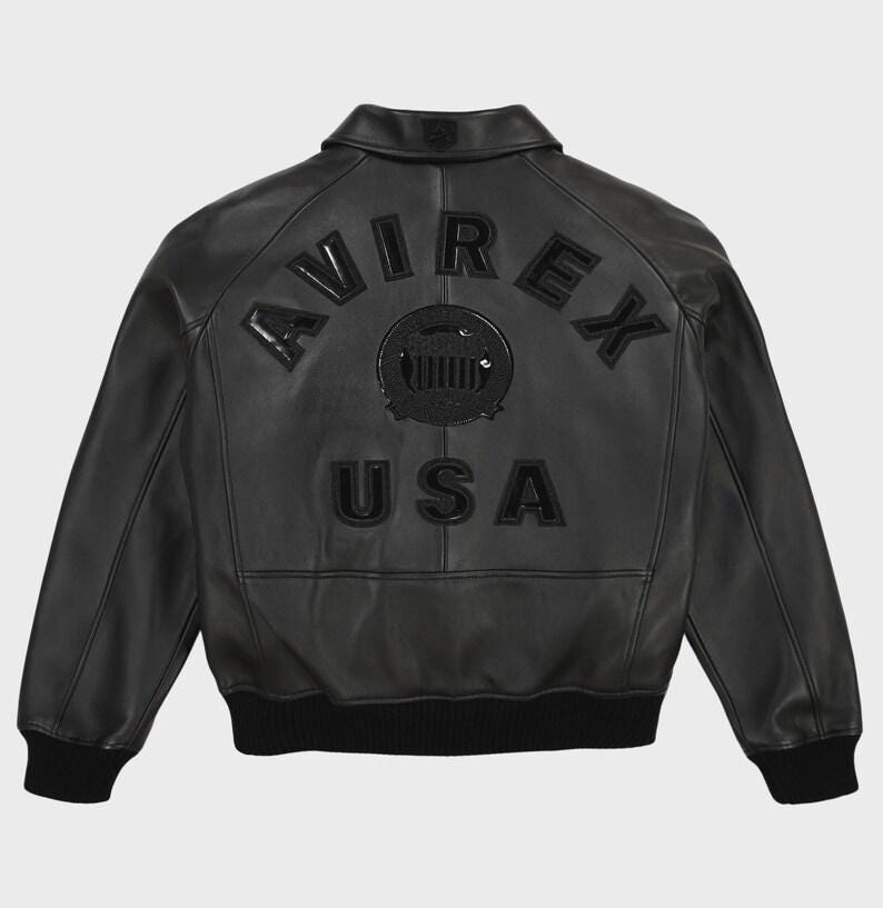May include: Black leather bomber jacket with the word "AVIREX" arched across the back, above a circular emblem and the word "USA". The jacket has a ribbed hem and cuffs, and a classic collar.