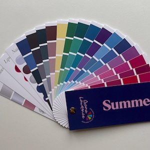 Puede incluir: Un abanico de paletas de colores con una gama de colores de verano. El abanico incluye varios tonos de azul, morado, rosa, verde y tonos neutros. Las palabras "Summer" y "Oxana Lawrence" están impresas en una tarjeta azul marino adjunta.