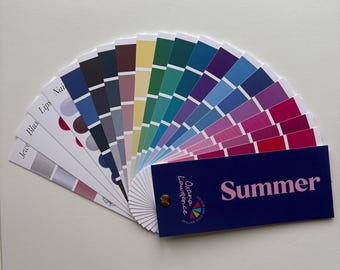 May include: A color palette fan featuring a range of summer-themed colors. The fan includes various shades of blue, purple, pink, green, and neutral tones. The words "Summer" and "Oxana Lawrence" are printed on a navy blue card attached to the fan.