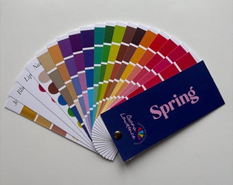 May include: A fan of color swatches with a variety of hues, including shades of yellow, pink, purple, and green. The fan includes a navy blue card with the word "Spring" in pink. The brand name "Oxana Lawrence" is also visible.