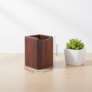 May include: A dark brown wooden desk organizer, 4.13 inches tall and 2.95 inches wide, with a square shape and a curved top opening. A small succulent in a white square pot sits next to it.