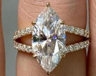 May include: A marquise-cut diamond engagement ring with a split shank band. The ring features a large, clear marquise-cut diamond as the centerpiece, with smaller diamonds set along the band. The ring is set in gold.
