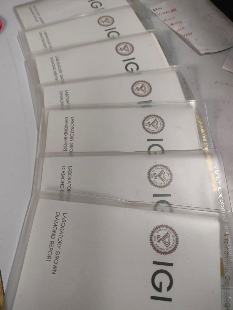 May include: A stack of white Laboratory Grown Diamond Report cards in clear plastic sleeves. The cards have the IGI logo and text. The cards are arranged in a slightly angled, overlapping pattern.