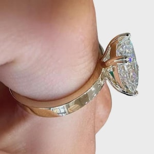 May include: A gold ring with a large, pear-shaped diamond. The diamond is clear and multifaceted, reflecting light. The ring's band is smooth and polished, with a classic design. The setting securely holds the diamond, showcasing its brilliance.